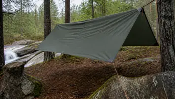 Mørkegrønn tarp stramt spent mellom furutrær ved en liten elv