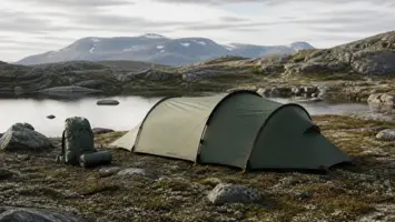 Lavt tunneltelt med ryggsekk ved et fjellvann på norsk høyfjell